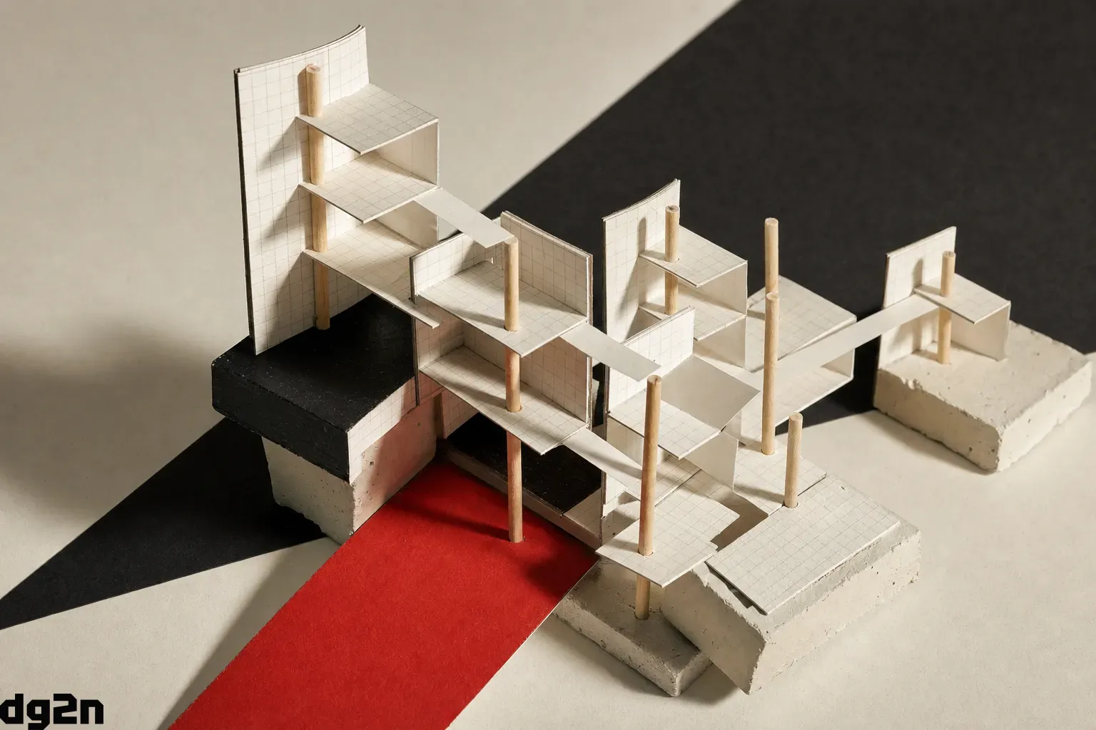 A physical architectural study model made of folded gridded paper, slender wooden rods, and plaster bases forming a modular tiered structure with connected joints.